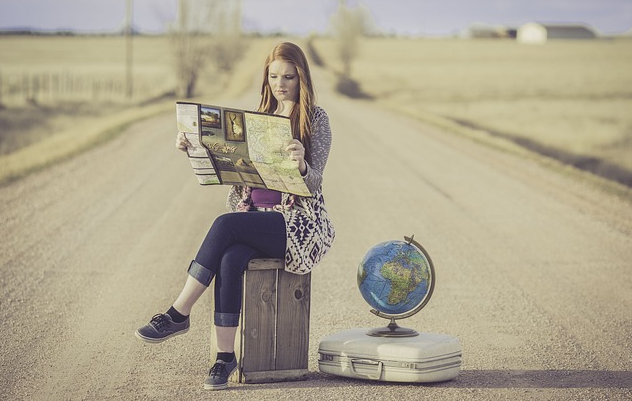 A woman sitting on a stool on a road with a world globe next to her. 